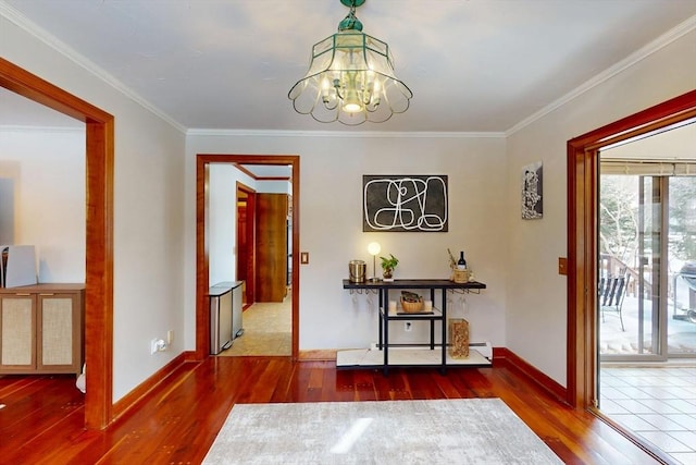 hall with a chandelier, a baseboard heating unit, wood finished floors, baseboards, and crown molding