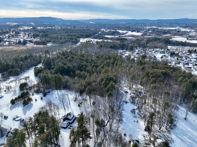 snowy aerial view with a wooded view and a mountain view