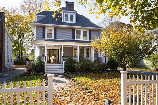 american foursquare style home featuring covered porch, a fenced front yard, a chimney, and a shingled roof