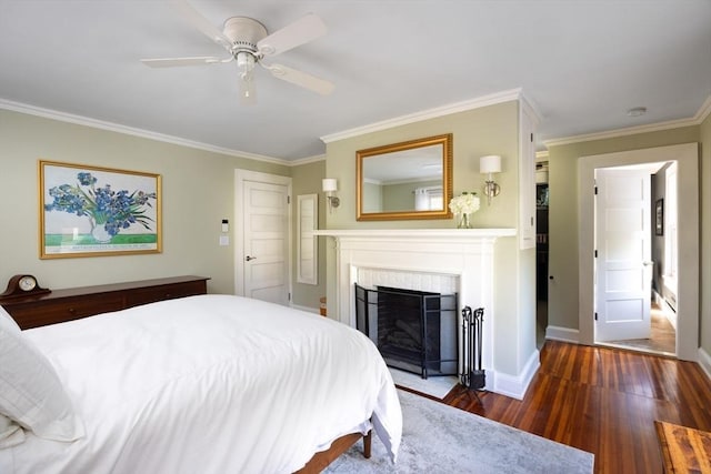 bedroom with ceiling fan, a fireplace, wood finished floors, baseboards, and crown molding