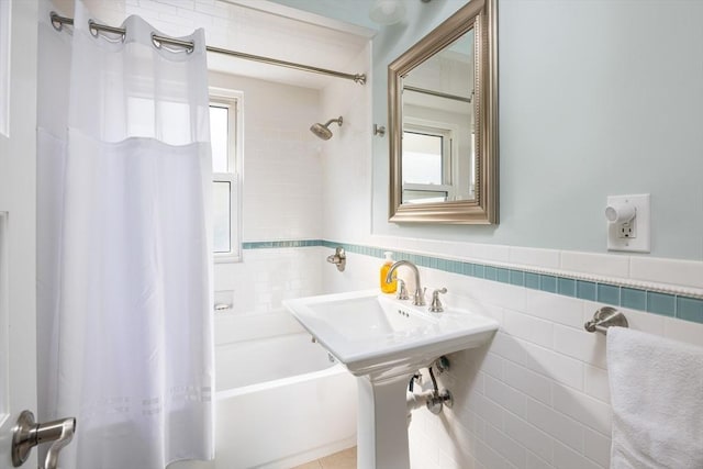 bathroom with a wainscoted wall, shower / bath combo with shower curtain, and tile walls