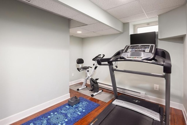 exercise area featuring baseboard heating, wood finished floors, a paneled ceiling, and baseboards