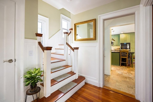 stairs with a wainscoted wall, wood finished floors, and a decorative wall