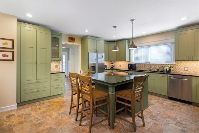 kitchen with dark stone counters, green cabinetry, stainless steel appliances, a kitchen bar, and a sink