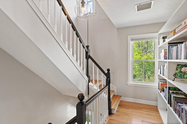 stairway featuring baseboards, a textured ceiling, wood finished floors, and visible vents