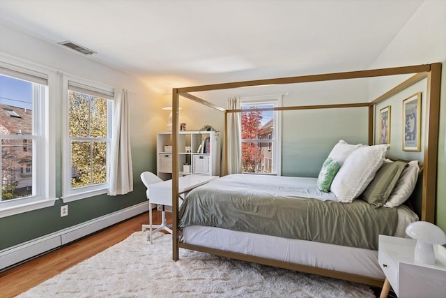bedroom featuring baseboards, visible vents, wood finished floors, and a baseboard radiator
