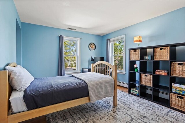 bedroom with baseboard heating, wood finished floors, and visible vents