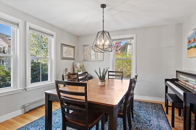 dining space featuring a notable chandelier, a healthy amount of sunlight, baseboard heating, and wood finished floors
