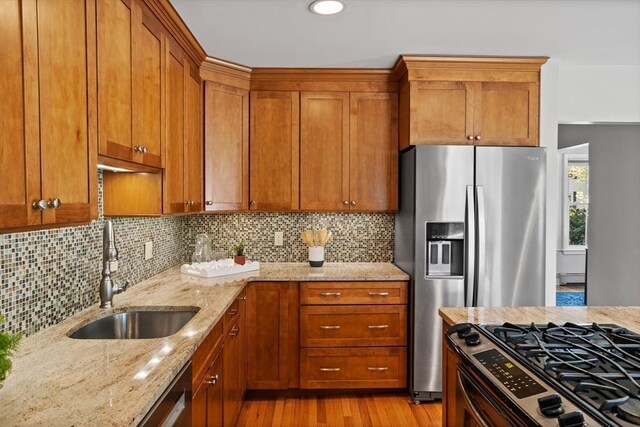 kitchen featuring a sink, brown cabinets, light stone countertops, and stainless steel appliances