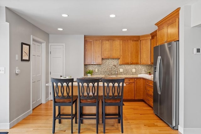 kitchen with light wood finished floors, a kitchen breakfast bar, recessed lighting, tasteful backsplash, and stainless steel refrigerator with ice dispenser