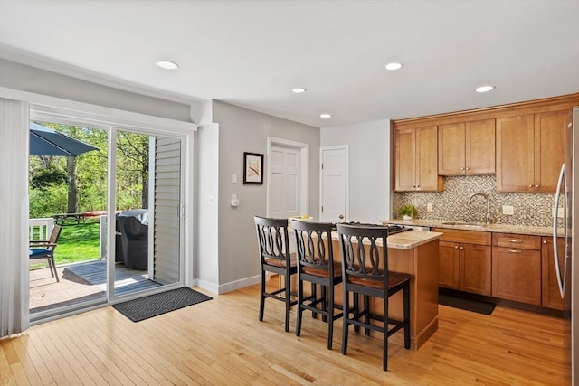 kitchen with a sink, light wood finished floors, backsplash, and a kitchen island
