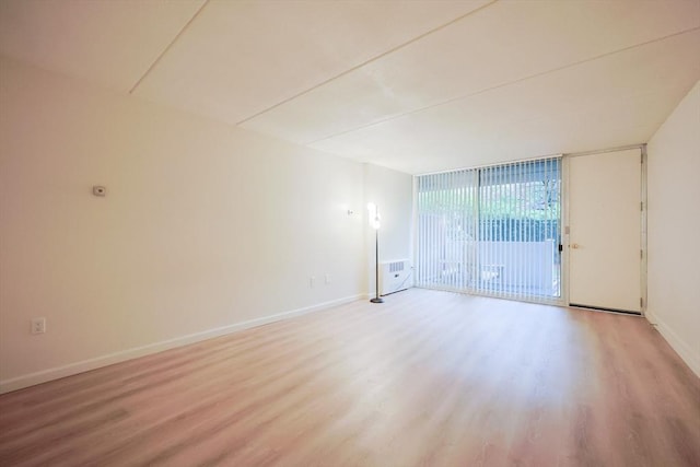 unfurnished room featuring light wood-type flooring, baseboards, and a wall of windows