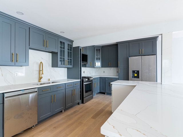 kitchen featuring stainless steel appliances, light stone countertops, light wood-type flooring, sink, and backsplash