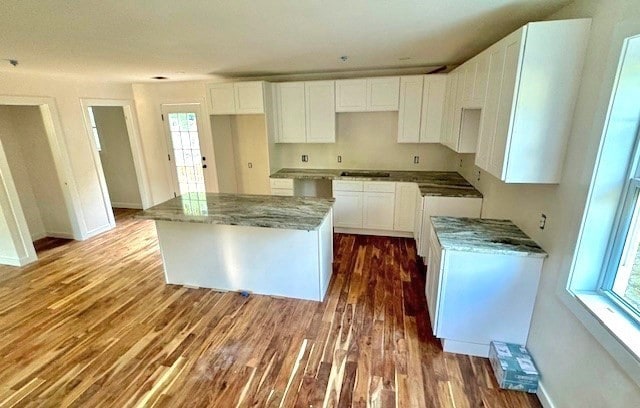 kitchen featuring white cabinetry, a center island, wood-type flooring, and light stone counters