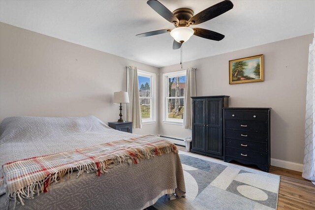 bedroom featuring a ceiling fan, baseboards, baseboard heating, and wood finished floors