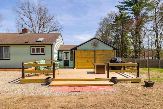 back of property with fence, a wooden deck, a chimney, and a shingled roof