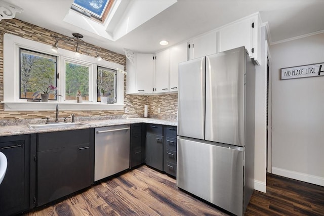 kitchen with a sink, a skylight, backsplash, and stainless steel appliances