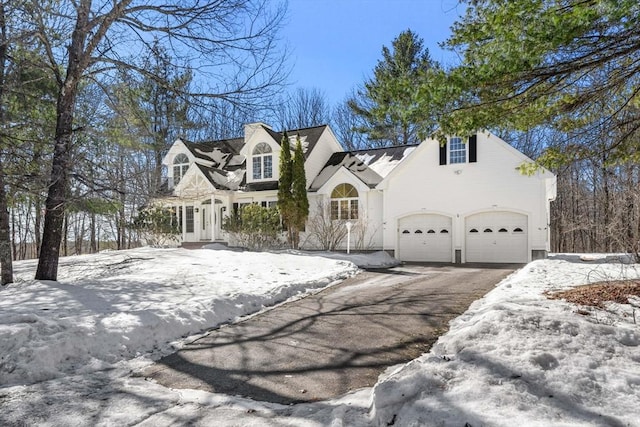 cape cod-style house featuring driveway, a garage, and a chimney