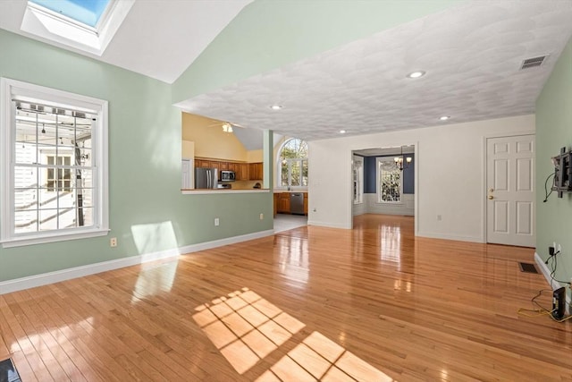 unfurnished living room with vaulted ceiling with skylight, a wealth of natural light, light wood-type flooring, and visible vents