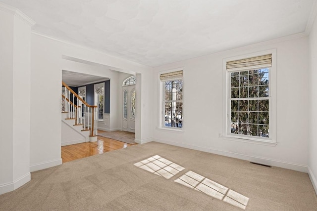 empty room with carpet, crown molding, visible vents, baseboards, and stairs