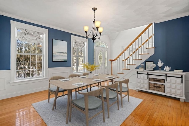 dining room with wainscoting, wood-type flooring, stairway, ornamental molding, and an inviting chandelier