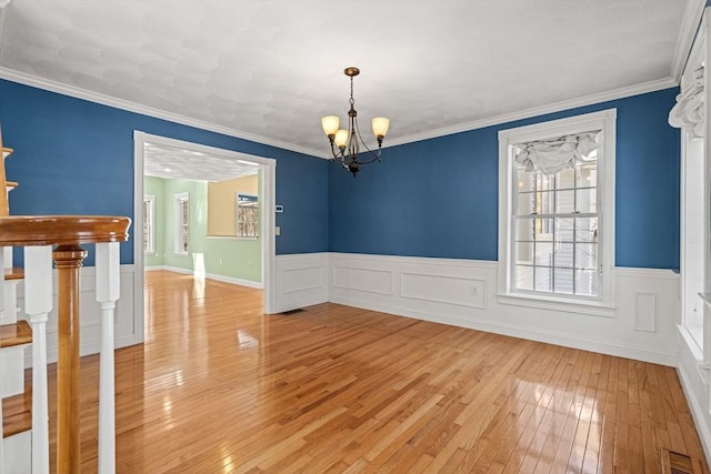 unfurnished room with visible vents, wainscoting, ornamental molding, light wood-type flooring, and a chandelier