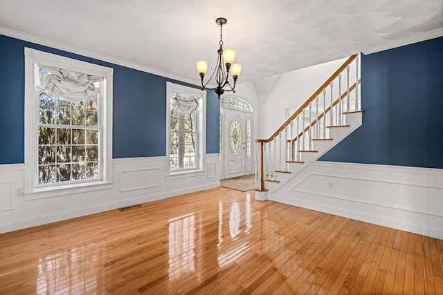 foyer entrance with visible vents, ornamental molding, hardwood / wood-style floors, stairs, and a chandelier