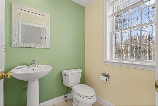 half bath with baseboards, a healthy amount of sunlight, a sink, and toilet