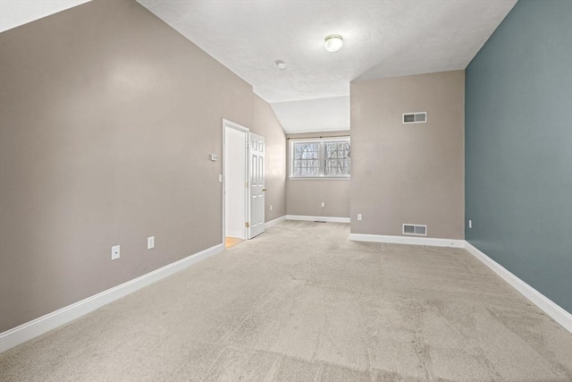 empty room with visible vents, vaulted ceiling, light carpet, and baseboards