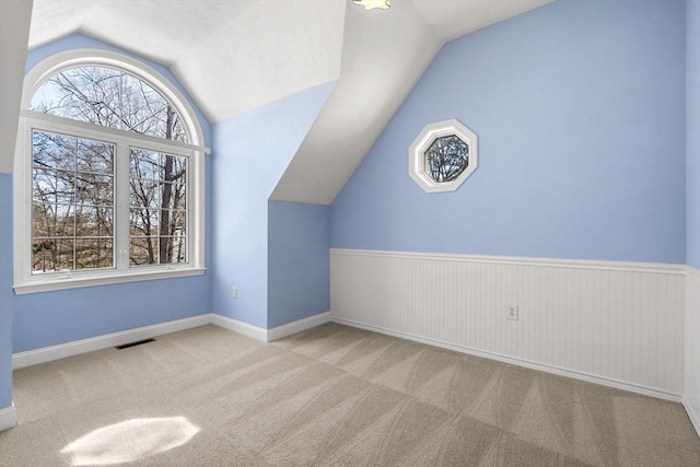 additional living space featuring baseboards, visible vents, wainscoting, vaulted ceiling, and carpet flooring