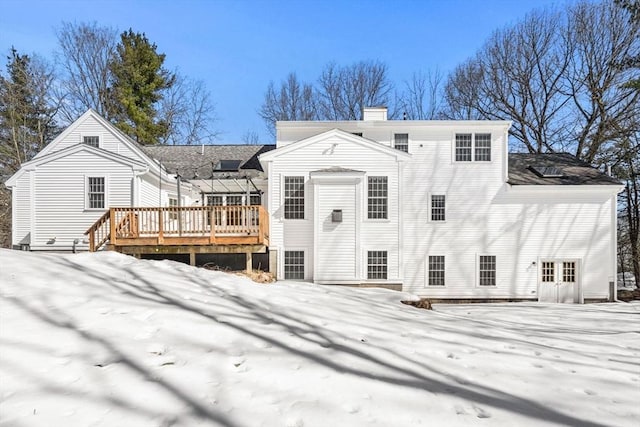 snow covered back of property featuring a chimney and a wooden deck