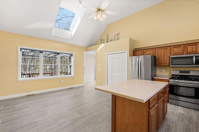 kitchen with a skylight, brown cabinets, light countertops, appliances with stainless steel finishes, and a kitchen island