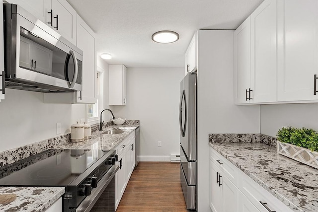 kitchen with stainless steel appliances, light stone counters, a sink, and white cabinetry