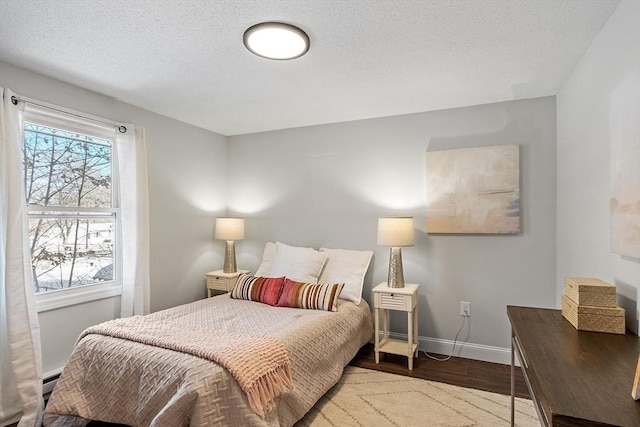 bedroom featuring multiple windows, a textured ceiling, baseboards, and wood finished floors