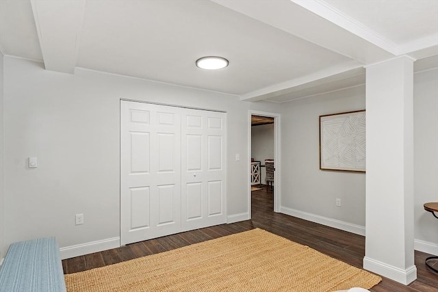 unfurnished bedroom with dark wood-style floors, crown molding, a closet, beamed ceiling, and baseboards