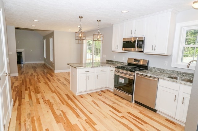 kitchen featuring stainless steel appliances, sink, white cabinetry, light hardwood / wood-style floors, and kitchen peninsula