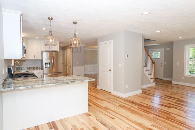 kitchen with light stone counters, kitchen peninsula, stainless steel appliances, and light hardwood / wood-style floors