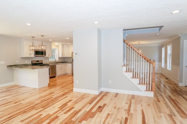 kitchen featuring stainless steel appliances, kitchen peninsula, white cabinetry, light hardwood / wood-style flooring, and decorative light fixtures