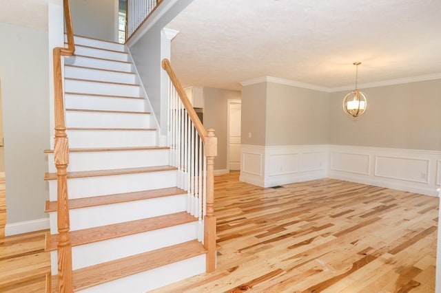 staircase with a notable chandelier, crown molding, and hardwood / wood-style flooring