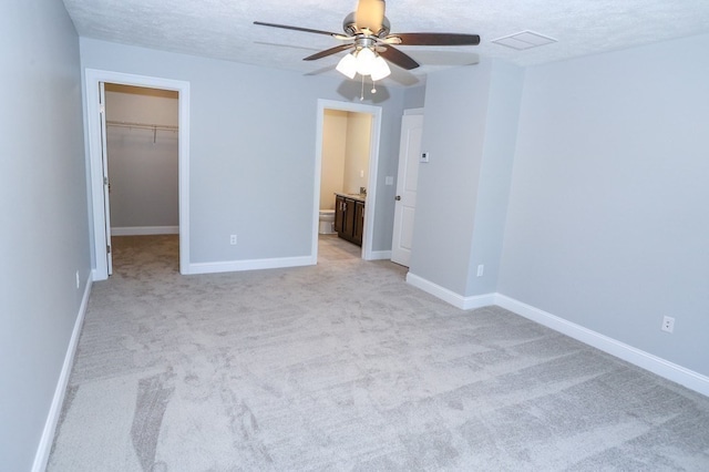 unfurnished bedroom with ceiling fan, a spacious closet, a closet, and light colored carpet