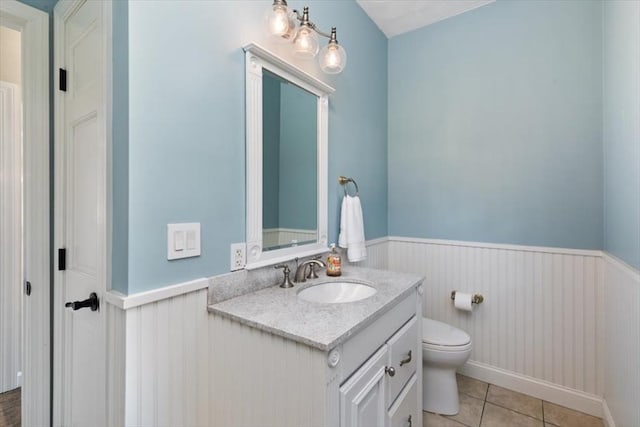 half bathroom with vanity, tile patterned floors, toilet, and a wainscoted wall