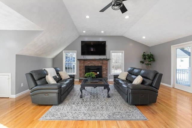 living room featuring wood finished floors, baseboards, ceiling fan, vaulted ceiling, and a brick fireplace