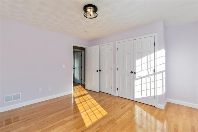 unfurnished bedroom featuring visible vents, baseboards, two closets, and light wood finished floors