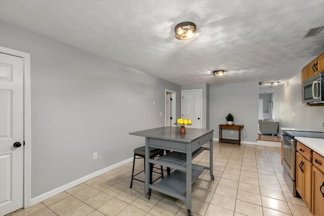 kitchen with light tile patterned floors, visible vents, appliances with stainless steel finishes, a textured ceiling, and brown cabinets