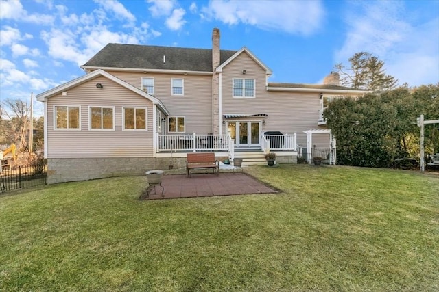 rear view of property featuring a lawn, fence, a wooden deck, a chimney, and a patio area