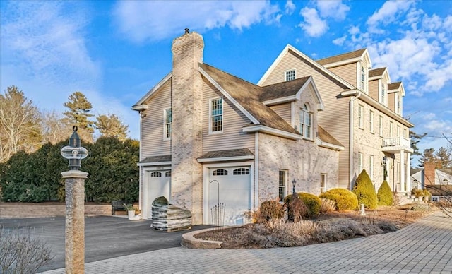 view of home's exterior with brick siding, driveway, a chimney, and a garage