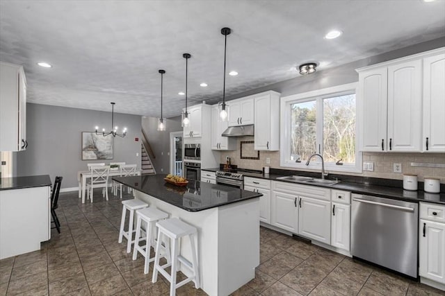 kitchen featuring a sink, under cabinet range hood, appliances with stainless steel finishes, dark countertops, and backsplash