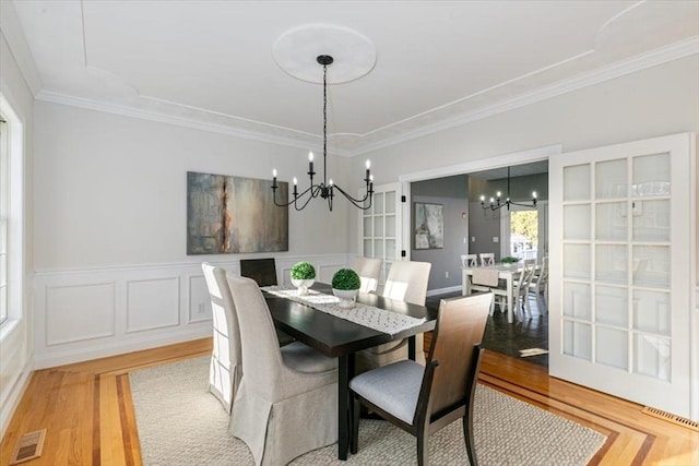 dining space featuring visible vents, a wainscoted wall, a notable chandelier, crown molding, and light wood finished floors