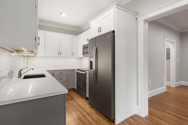 kitchen featuring light wood-type flooring, ornamental molding, a sink, appliances with stainless steel finishes, and light countertops