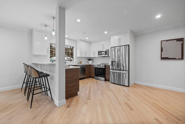 kitchen featuring a breakfast bar, white cabinetry, stainless steel appliances, light hardwood / wood-style floors, and backsplash